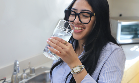 Woman drinking fresh and clean water from a cup in her kitchen
